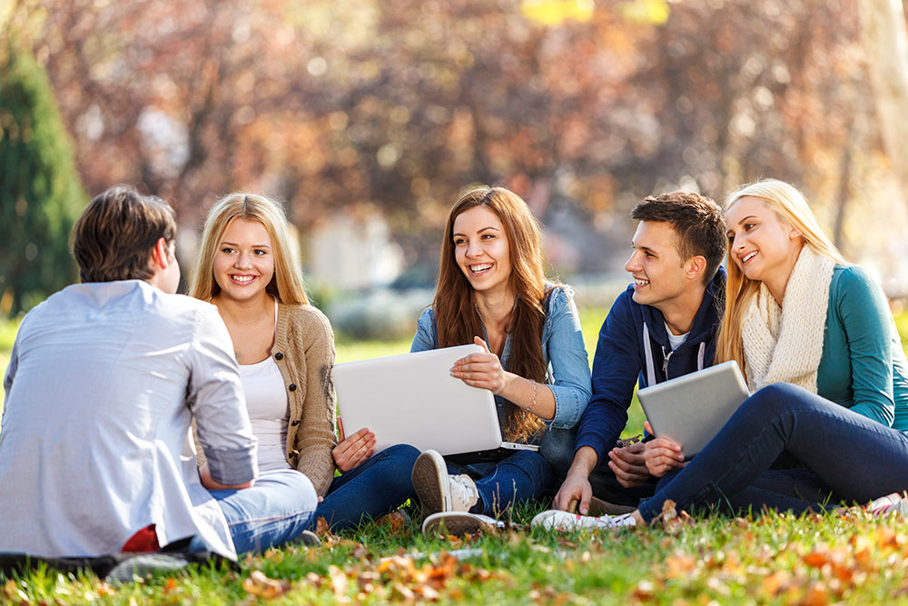 Group of teenagers sitting on grass and talking.